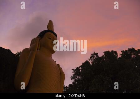 Une vue en bas angle d'un grand bouddha maigre doré devant un beau ciel de coucher de soleil dans un temple à Unawatuna, Sri Lanka. Horizontal Banque D'Images