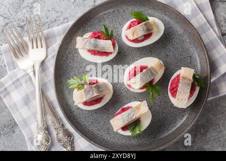 Œufs dévorés festifs farcis de betteraves et de hareng gros plan dans une assiette sur la table. Vue horizontale de dessus Banque D'Images