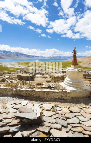 Korzok, Inde, 3 août 2013 : inscriptions tibétaines sur des pierres derrière des stupas avec vue panoramique sur le village du lac de haute altitude Tso Moriri en été à L. Banque D'Images