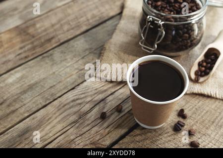 Concept de petit déjeuner au café avec une tasse de papier de café noir expresso, café torréfié sec grains dans le pot en verre et cuillère à l'ancienne table en bois Banque D'Images
