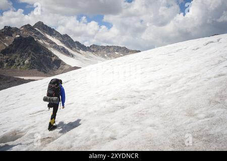 Un alpiniste avec un sac à dos marche dans des crampons marchant le long d'un glacier poussiéreux avec des trottoirs dans les mains entre les fissures dans la montagne Banque D'Images