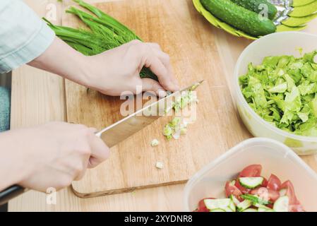 Gros plan des mains douces des femmes trancher sur la planche de bois les tiges d'oignons verts faisant de la salade. Le concept d'un aliment végétarien sain et vivant Banque D'Images