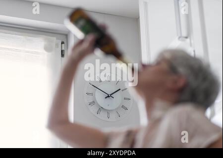 Une femme se tient dans la cuisine à l'heure du déjeuner et boit une bouteille de bière Banque D'Images