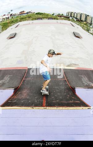 Jeune patineur faisant le tour sur une rampe sur une planche à roulettes dans un skate Park. Grand angle Banque D'Images