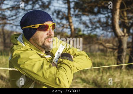 Un portrait en gros plan d'homme sage et expérimenté en âge avec des lunettes de soleil et portant un chapeau qui marchait sur une slackline et s'appuyait sur lui en méditation Banque D'Images