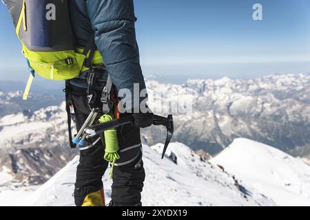 Gros plan Un jeune grimpeur tient dans sa main une hache de glace debout sur le sommet haut dans les montagnes sur fond de caucasien enneigé Banque D'Images