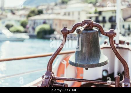 Proue d'un bateau avec cloche de bateau lors d'une croisière. Eau bleue, chaîne de montagnes et mignon petit village à Lago di Garda, Italie, Europe Banque D'Images