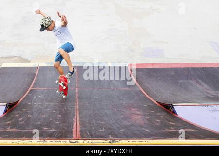 Adolescent patineur raccroché au-dessus d'une rampe sur une planche à roulettes dans un skate Park. Grand angle Banque D'Images