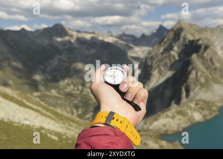 La main d'un homme tient une boussole magnétique de poche pour la navigation sur la toile de fond d'une pente rocheuse et d'un lac de montagne. Le concept de trouver un moyen. G Banque D'Images