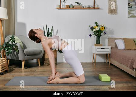 Une femme dans un crop top pratique le yoga à la maison, agenouillée sur un tapis avec la tête en arrière, dans un appartement moderne. Banque D'Images