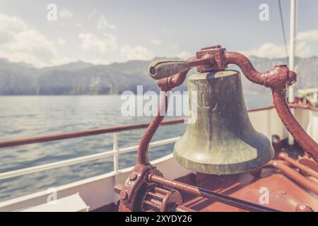 Proue d'un bateau avec cloche de bateau lors d'une croisière. Eau bleue, chaîne de montagnes et mignon petit village à Lago di Garda, Italie, Europe Banque D'Images