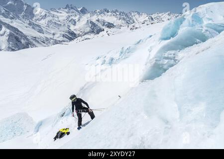 Un alpiniste professionnel portant un casque et un masque de ski sur l'assurance entaille la hache de glace dans le glacier. Le travail d'un grimpeur professionnel en Winte Banque D'Images