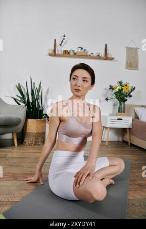 Une jeune femme asiatique dans un crop top pratique le yoga et la méditation sur un tapis dans un appartement moderne. Banque D'Images