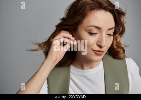 Une femme asiatique élégante portant un gilet ajuste sa boucle d'oreille tout en regardant vers le bas. Banque D'Images