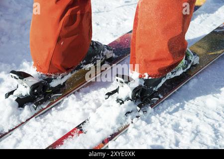 Chaussures de ski alpin orange dans une monture de ski. Une chaussure est complètement fixée sur les skis, la seconde ne l'est pas. Gros plan. Costume orange Banque D'Images
