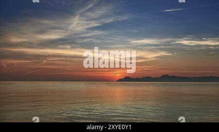 Coucher de soleil marin orange coloré sur un océan calme et des collines lointaines au crépuscule avec la lumière du soleil couchant se reflétant sur l'océan Banque D'Images