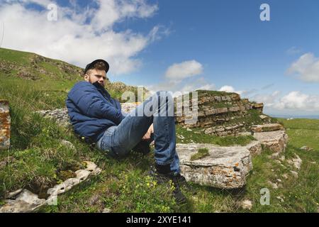 Portrait d'un homme barbu joyeux en bonnet gris avec des fleurs sauvages dans une barbe. Douce brutalité et bonne masculinité. Repose dans une veste sur l'herbe dans le Banque D'Images