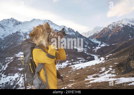 Portrait d'une fille de touriste douce dans un grand chapeau de fourrure prend des photos sur son appareil photo reflex numérique dans les montagnes. En hiver le concept de photographie dans les voyages. Banque D'Images