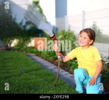 Petite fille d'arroser l'herbe dans le jardin Banque D'Images