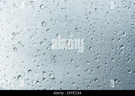 Fond texturé de vitres de fenêtre avec un fond nuageux. Motif naturel d'une goutte de pluie sur un fond nuageux Banque D'Images