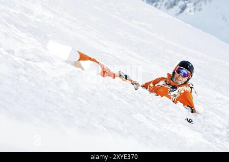 Un skieur dans une combinaison orange et avec un sac à dos se trouve heureux dans la neige après être tombé. Le concept de loisirs dans les montagnes et le ski Banque D'Images