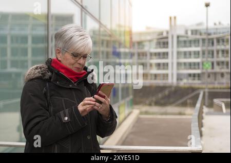 Une personne âgée aux cheveux courts et blancs se tient dans le Media Harbour de Duesseldorf et regarde son smartphone Banque D'Images