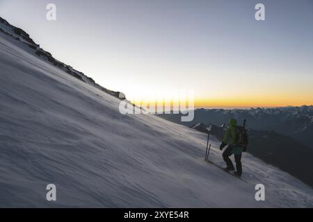 L'alpiniste professionnellement équipé à l'aube du soleil marche sur la pente au petit matin et la neige dérive sur la neige au-dessus de la neige. T Banque D'Images