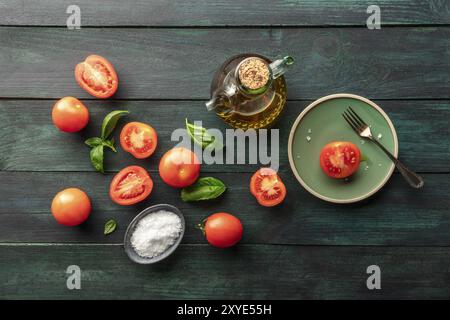 Organic heirloom tomatoes avec feuilles de basilic frais, tourné à partir de ci-dessus, sur un fond rustique foncé avec du sel, l'huile d'olive, et copy space Banque D'Images