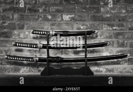 Sabre samouraï set japonais Katana Wakizashi et Tanto lames dans des fourreaux sur un fond de mur de briques grungy Sepia blanc noir Banque D'Images