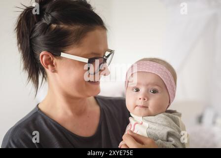 Mère tenant belle fille de bébé dans la chambre lumineuse ensoleillée. Arrière-plan de la maternité Banque D'Images