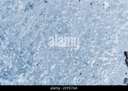 Gros plan de la surface d'un fragment d'un glacier avec une structure de bandes et de bulles entrecoupées de sable et de roches rocheuses. Texture bleu glacé à Banque D'Images