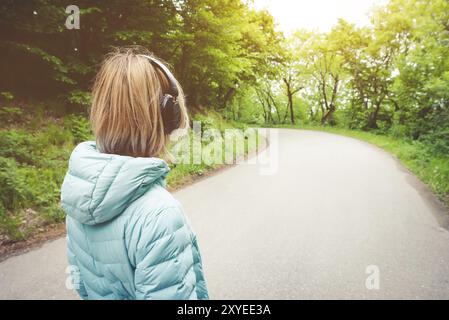 Portrait d'une fille blonde athlétique attrayante de dos à la lumière courir vers le bas veste, portant des écouteurs bluetooth avec de la musique ou des sons de la nature quand o Banque D'Images