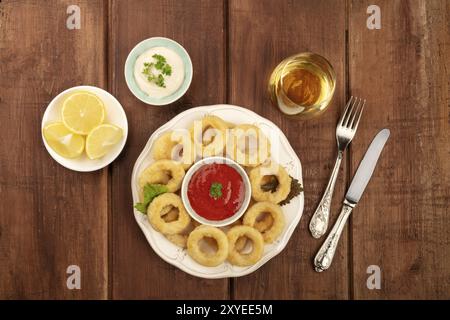 Un plan en plongée d'anneaux de calmars avec deux sauces, des quartiers de citron, du vin blanc, et un lieu pour le texte Banque D'Images