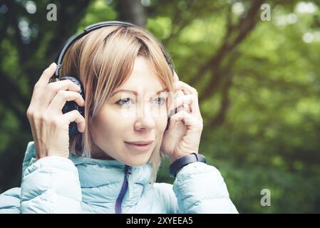 Portrait d'une fille de sport attrayante blonde dans une veste de descente légère habillant casque bluetooth avec de la musique ou les sons de la nature tout en étant sur Banque D'Images