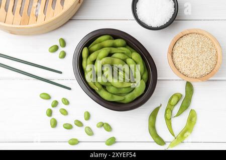 Gousses d'edamame fraîches, soja, sel et graines sur table en bois blanc, pose à plat Banque D'Images