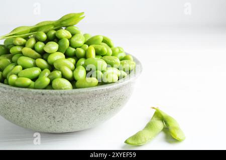 Soja edamame frais dans un bol et gousses sur une table en bois blanc, gros plan Banque D'Images