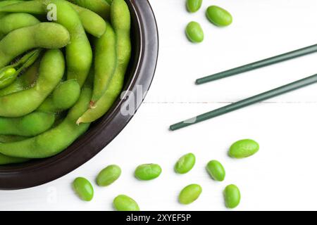 Gousses d'edamame fraîches, soja et baguettes sur table en bois blanc, pose à plat Banque D'Images