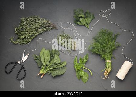 Différentes herbes fraîches, bobine de fil et ciseaux sur table texturée grise, pose à plat Banque D'Images