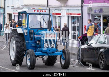 Homme conduisant un tracteur vintage Ford 4000 bleu à travers le centre-ville lors d'un événement de course de tracteur classique. Ballycastle, Royaume-Uni - 24 août 2024. Banque D'Images