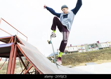 Un adolescent skateur dans un chapeau fait un tour avec un saut sur la rampe. Un skateur vole dans les airs Banque D'Images