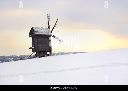 Ancien moulin à vent en rondins dans un champ couvert de neige silhouette solitaire sur le ciel du coucher du soleil Ukraine campagne d'Europe de l'est orientation horizontale panoramique d'hiver Banque D'Images