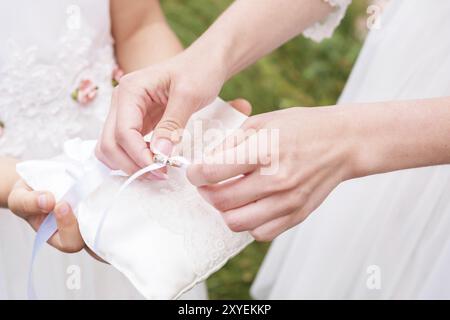 Demoiselle d'honneur à la main en robe blanche prend avec des anneaux de coussinets. Oreiller tient une petite fille demoiselle d'honneur Banque D'Images