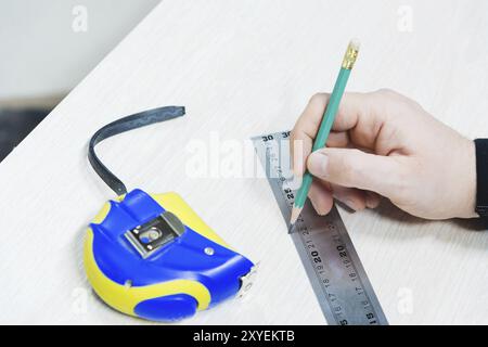 Gros plan Menuiserie, main de Mans à l'aide de ruban mesure pour mesurer la planche de bois et le marquage avec le crayon. Vue de dessus Banque D'Images