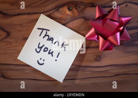 Une note qui dit "merci" est sur une surface en bois. Un arc rouge est placé à côté de la note Banque D'Images