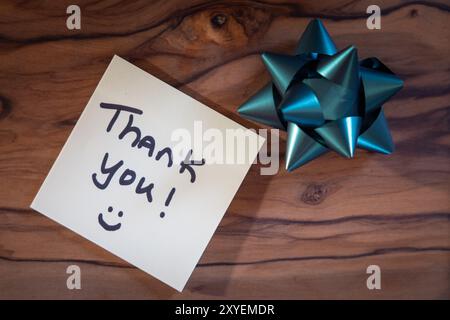 Une note qui dit "merci" est sur une surface en bois. Un arc bleu est placé à côté de la note Banque D'Images