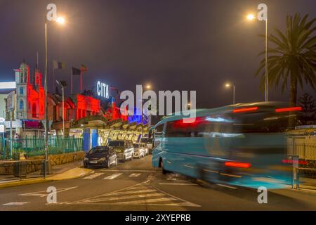 Prise de vue nocturne. Un autocar quitte un rond-point devant un centre commercial Banque D'Images