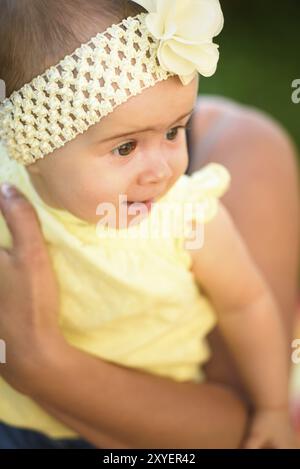 Portrait jeune mère tenant une petite fille mignonne dans un groupe et une robe jaunes. Journée d'été ensoleillée à l'extérieur. Concept de maternité Banque D'Images