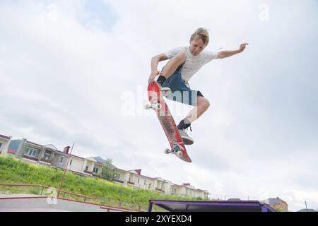 Jeune skateboarder intense en saut en hauteur contre le ciel et les zones de couchage Banque D'Images