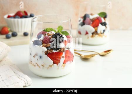 Yaourt savoureux avec baies fraîches, granola et menthe dans des verres servis sur une table blanche Banque D'Images