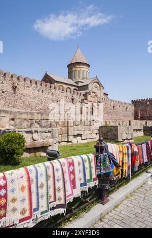 Tapis géorgiens faits à la main à vendre. L'église de Transfiguration derrière les portes fermées du monastère de Samtavro est en arrière-plan. Mtskheta, Géorgie Banque D'Images